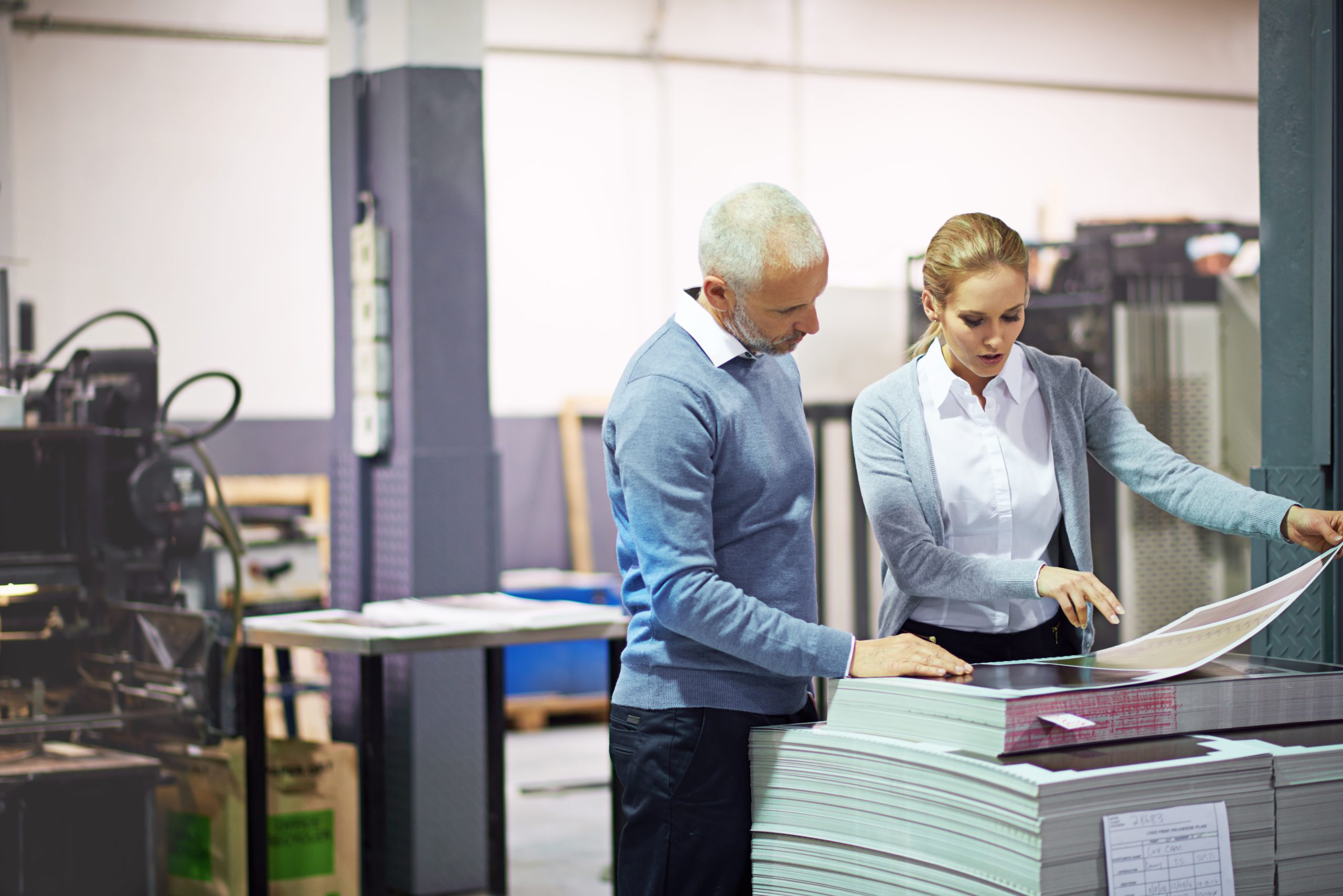 Shot of two managers looking over samples while standing inside a printing and packaging plant.